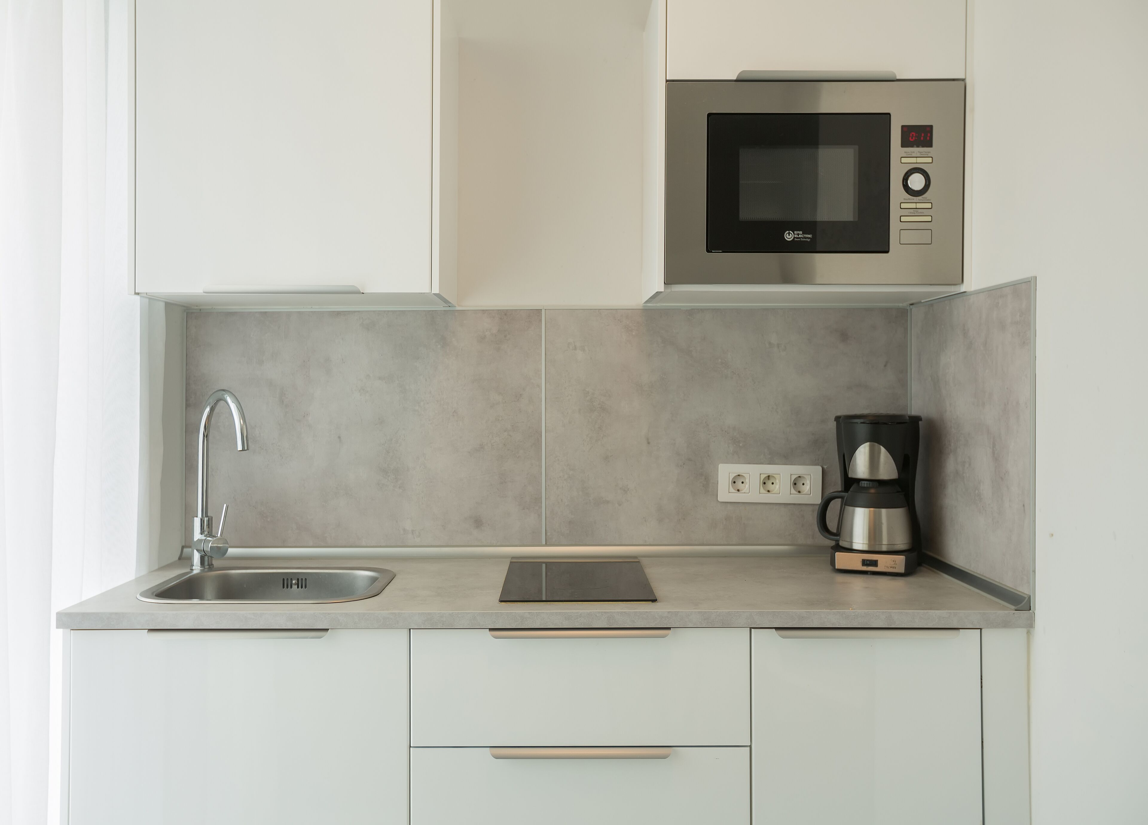 Una cucina moderna con lavandino in acciaio inossidabile, forno a microonde integrato e macchina per il caffè.