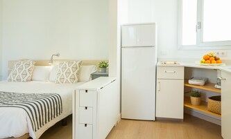 A compact hotel room with a bed, a small kitchenette, a refrigerator, and a window.