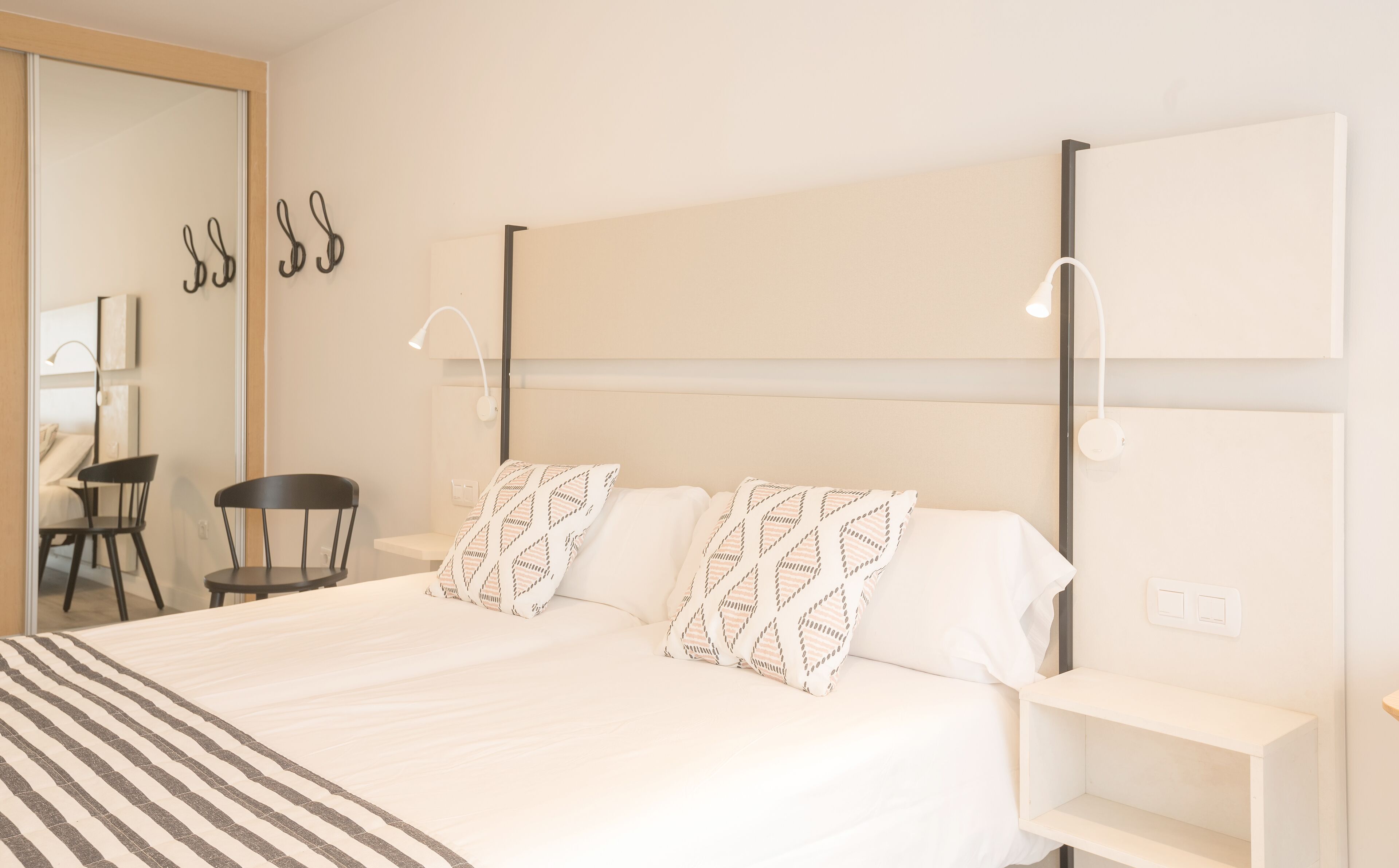 A hotel room with a large bed, two bedside tables, a chair, a desk, and a mirror.