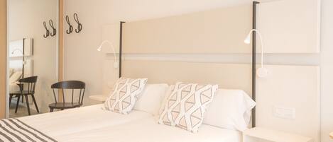 A hotel room with a large bed, two bedside tables, a chair, a desk, and a mirror.