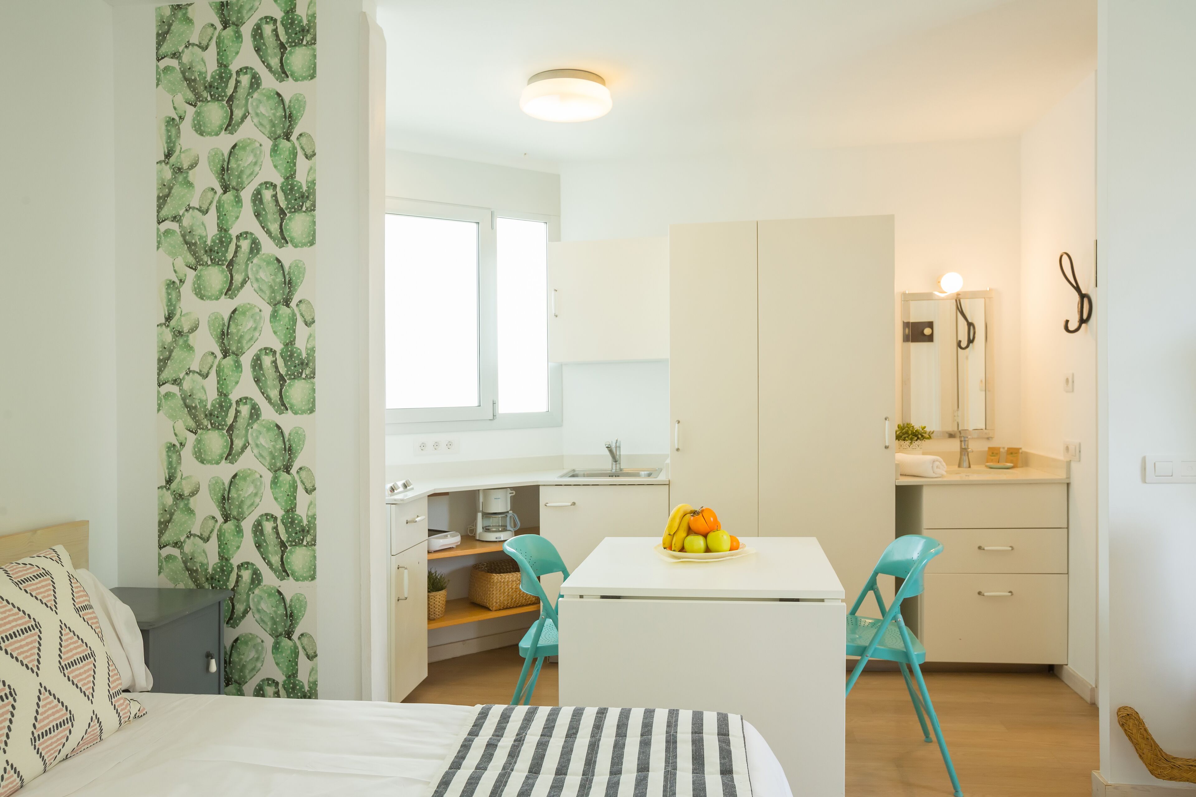 Ein kompakter, gut beleuchteter Raum mit einem Bett, einer kleinen Küchenzeile und einem Essbereich mit Tisch und Stühlen.