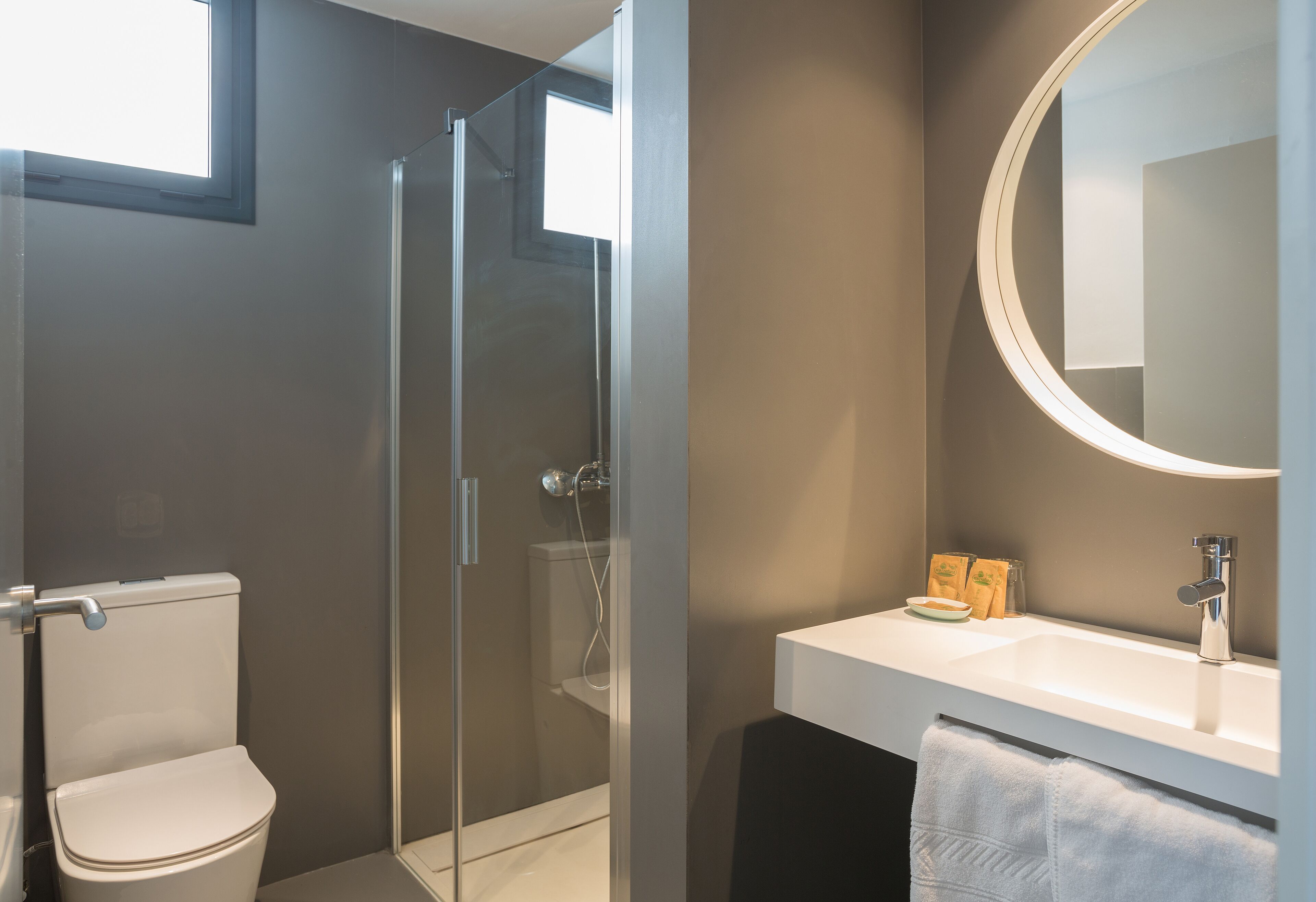 Une salle de bain moderne avec une douche à l’italienne en verre, un lavabo blanc et un grand miroir.