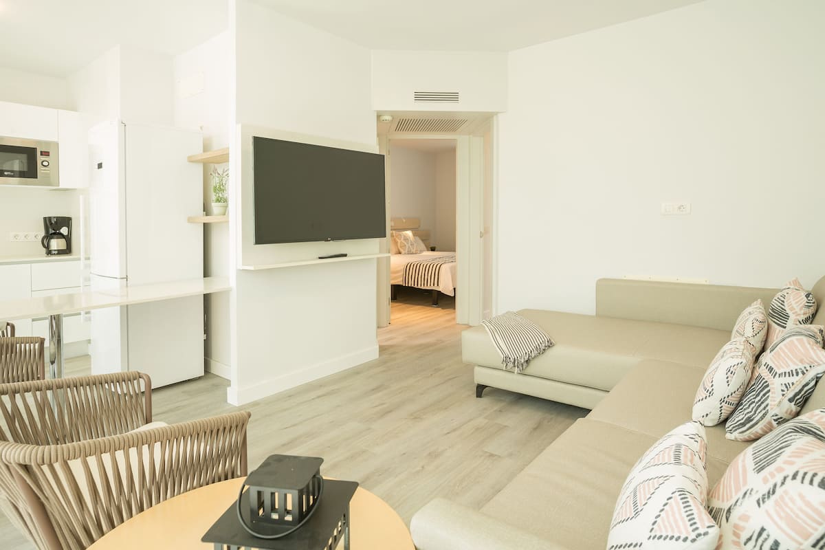 Una sala de estar moderna con un sofá, una mesa de centro y un televisor. Cuenta con una zona de cocina equipada con microondas y cafetera.
