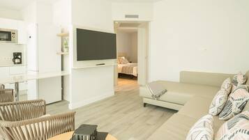 Una sala de estar moderna con un sofá, una mesa de centro y un televisor. Cuenta con una zona de cocina equipada con microondas y cafetera.