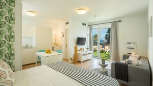 Una camera d'albergo con un letto, una scrivania con una ciotola di frutta, una televisione, un balcone vista mare e un divano.