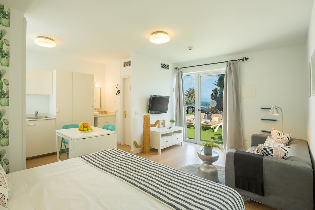 Habitación de hotel con cama, escritorio con frutero, televisor, balcón con vista al mar y sofá.
