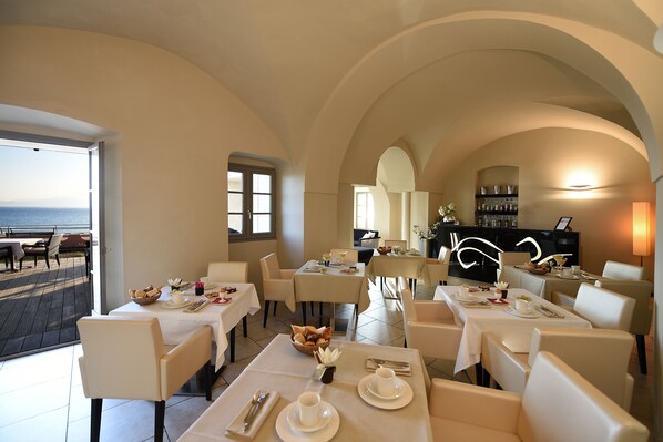 A dining area with tables set for meals, a bar area, and a view of the sea. - Hôtel Perla Rossa (L'Île-Rousse)