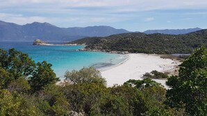 A coastal landscape with a sandy beach, clear turquoise waters, and a backdrop of mountains. - Hôtel Perla Rossa (L'Île-Rousse)