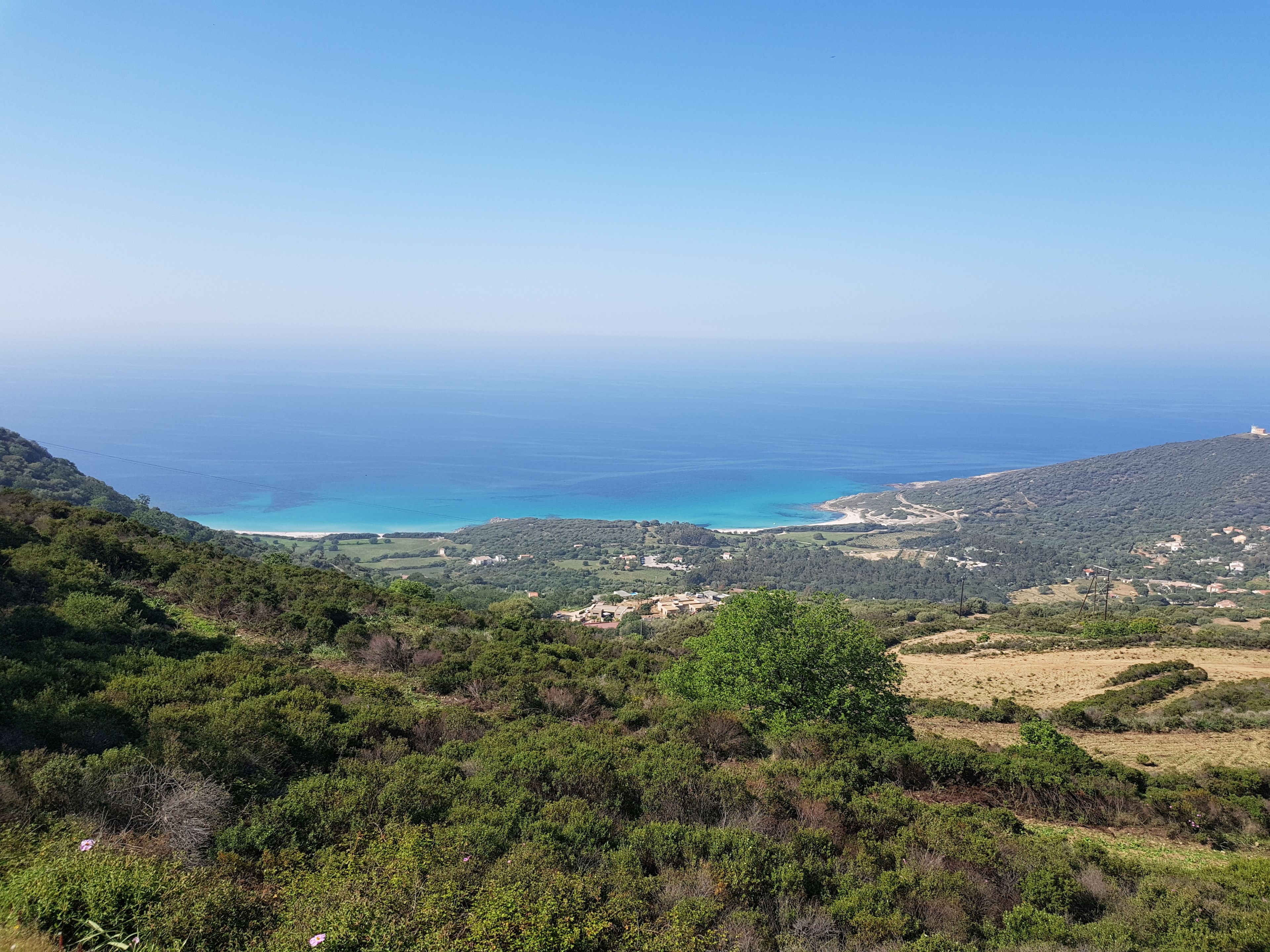 Un paysage côtier offrant une vue sur la mer, des collines et quelques bâtiments dispersés.