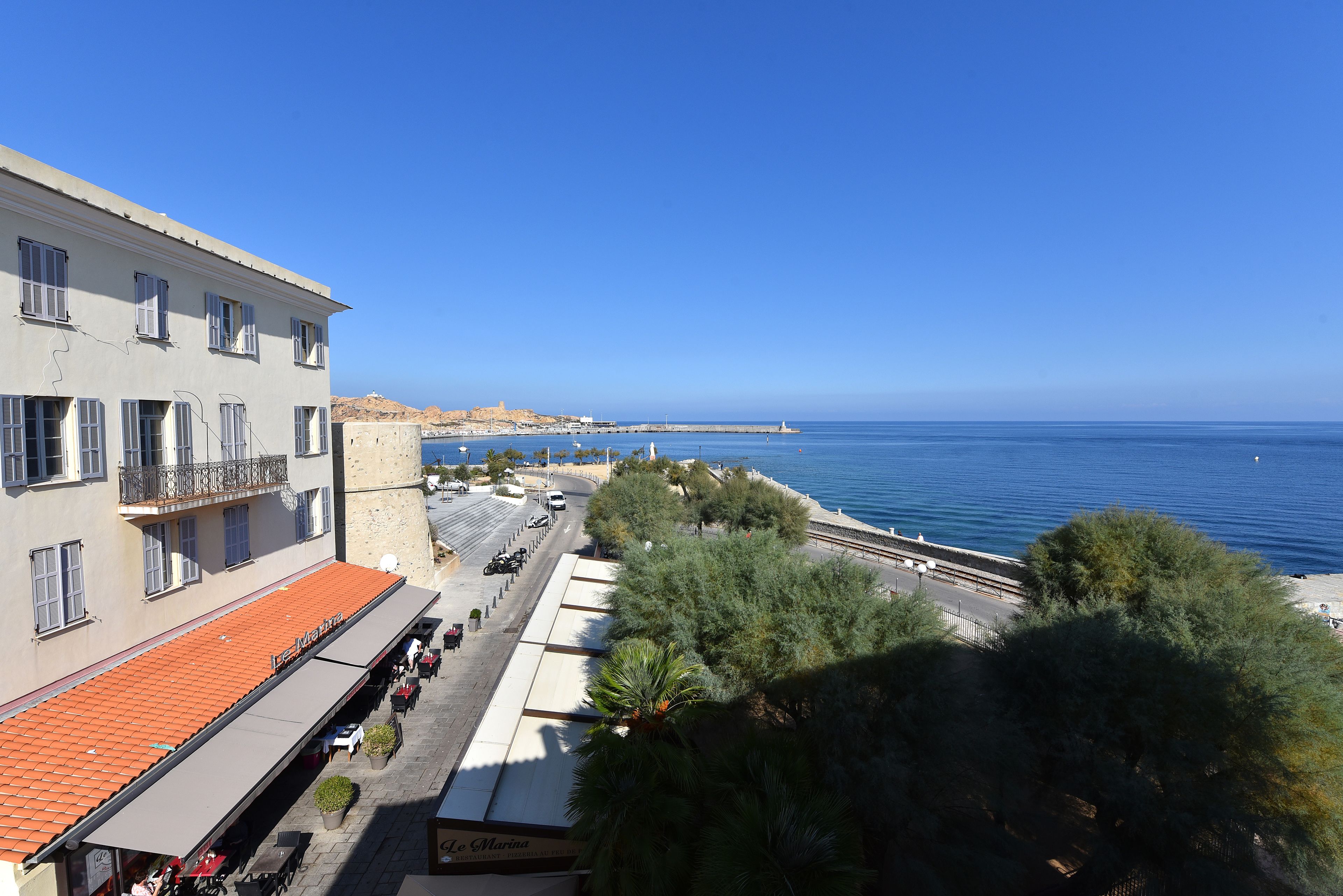 A coastal building with a red-tiled roof, a balcony, and a view of the sea.