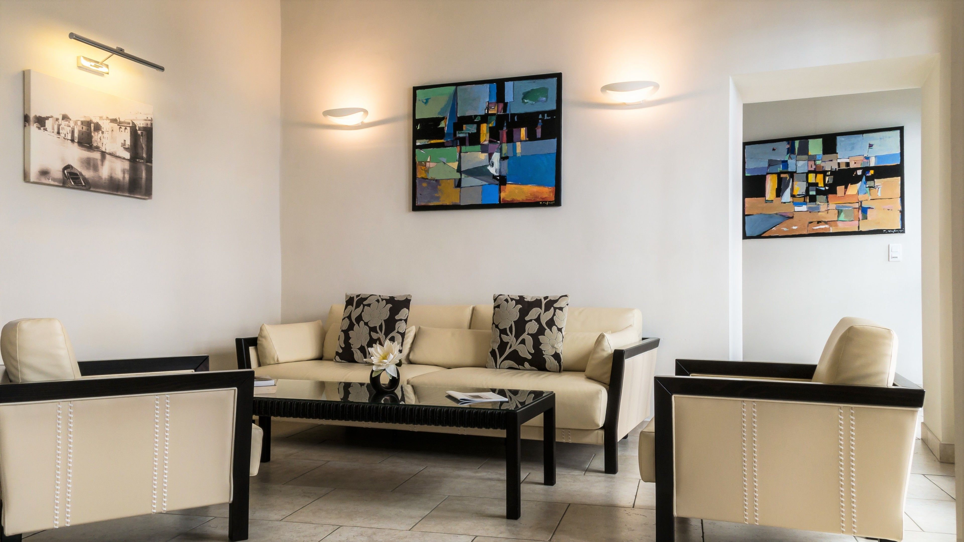 A living room with a sofa, two armchairs, a coffee table, and abstract paintings on the walls.