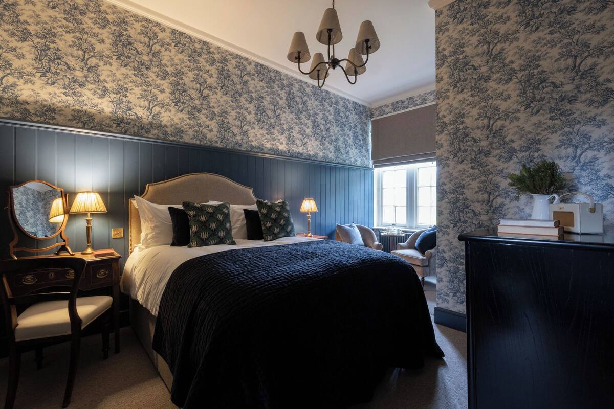 A bedroom with a large bed, two bedside tables with lamps, a dresser, and a chair.