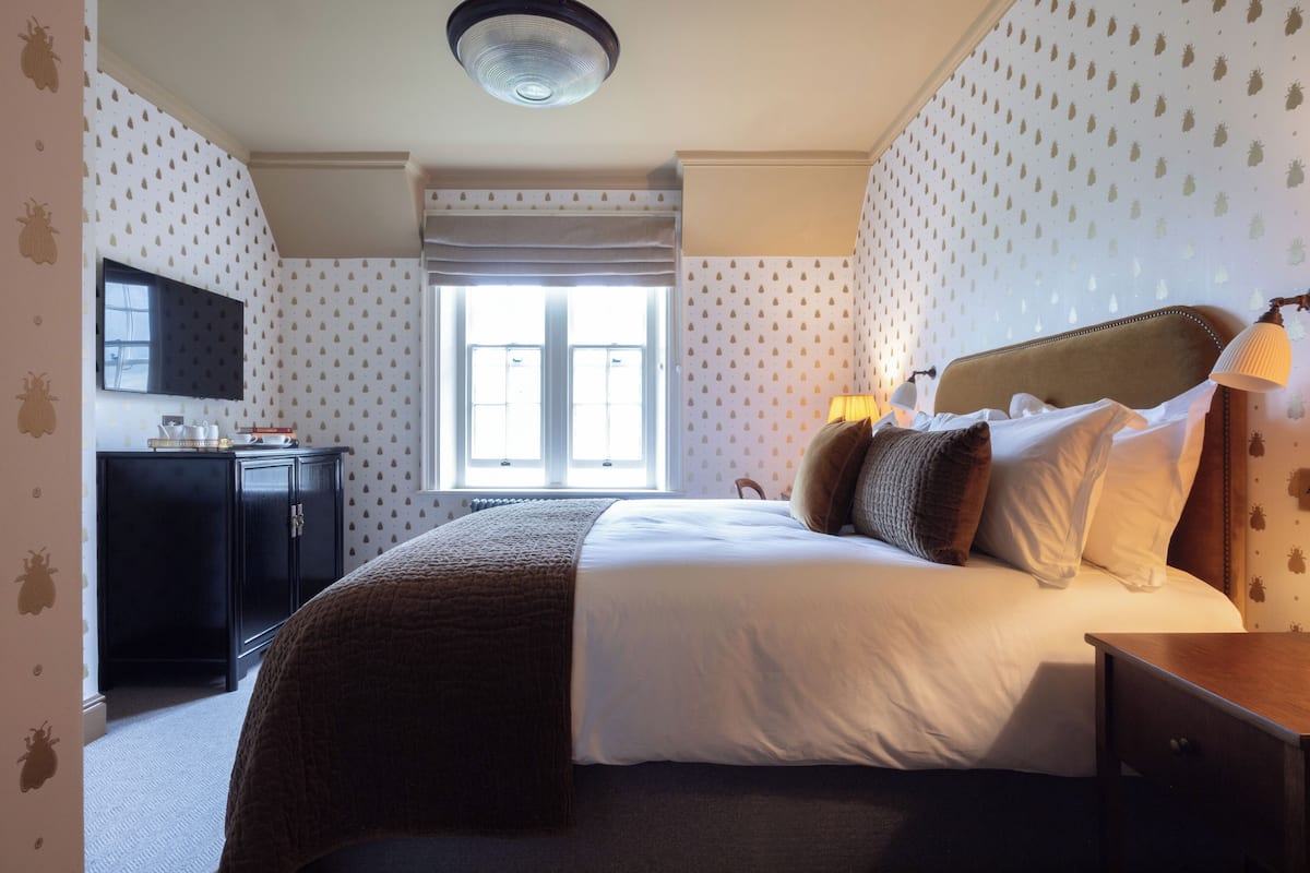 A neatly arranged bedroom with a bed, bedside table, lamp, and a TV on the wall.