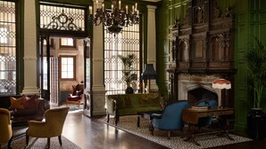 Um quarto amplo com parede verde, lareira, lustre e área de estar com sofá e cadeiras.