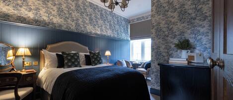 A bedroom with a large bed, two bedside tables with lamps, a chair, and a dresser.
