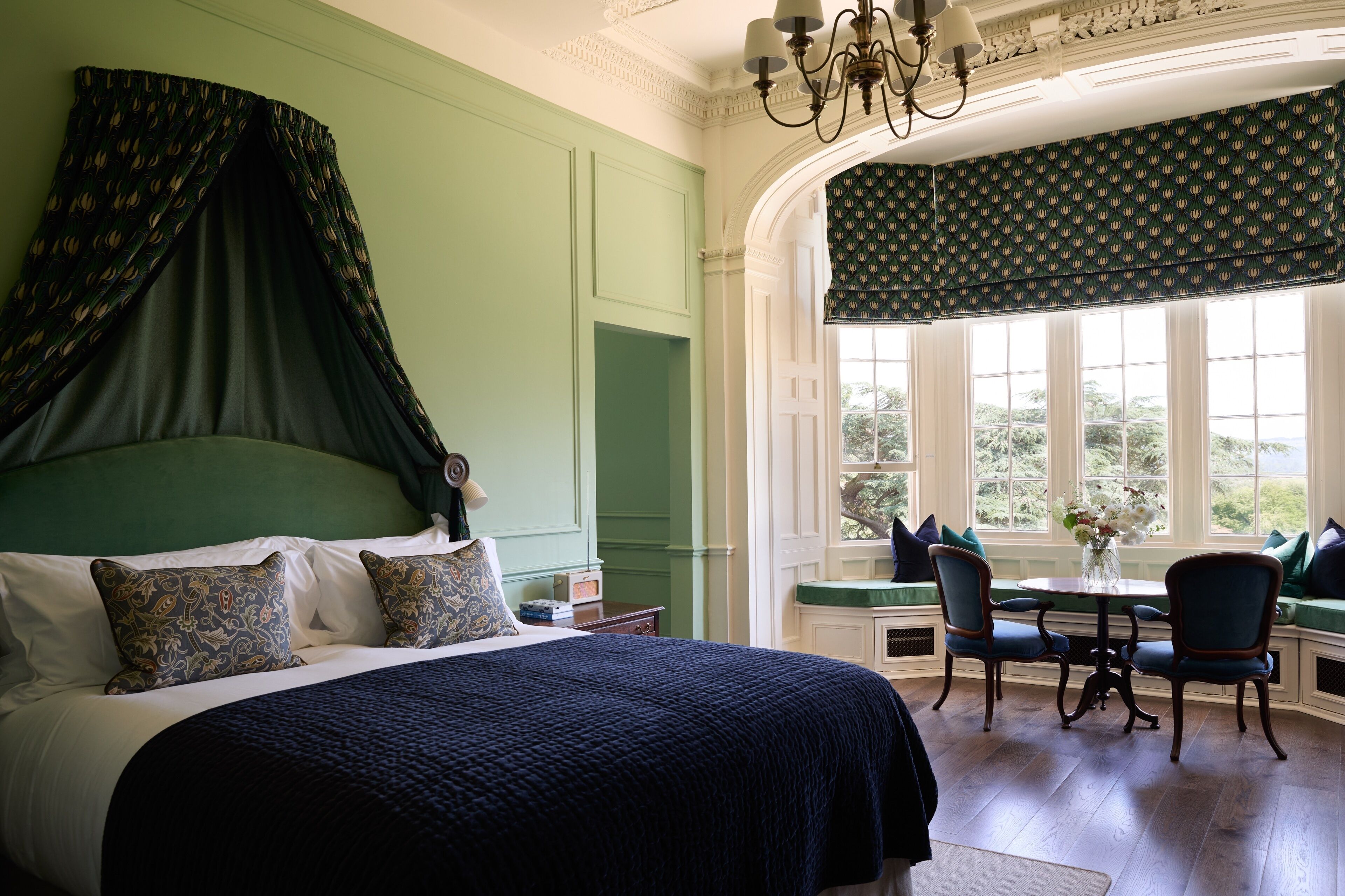 Un dormitorio con una cama grande, una mesa de comedor con sillas y vistas a zonas verdes por la ventana.