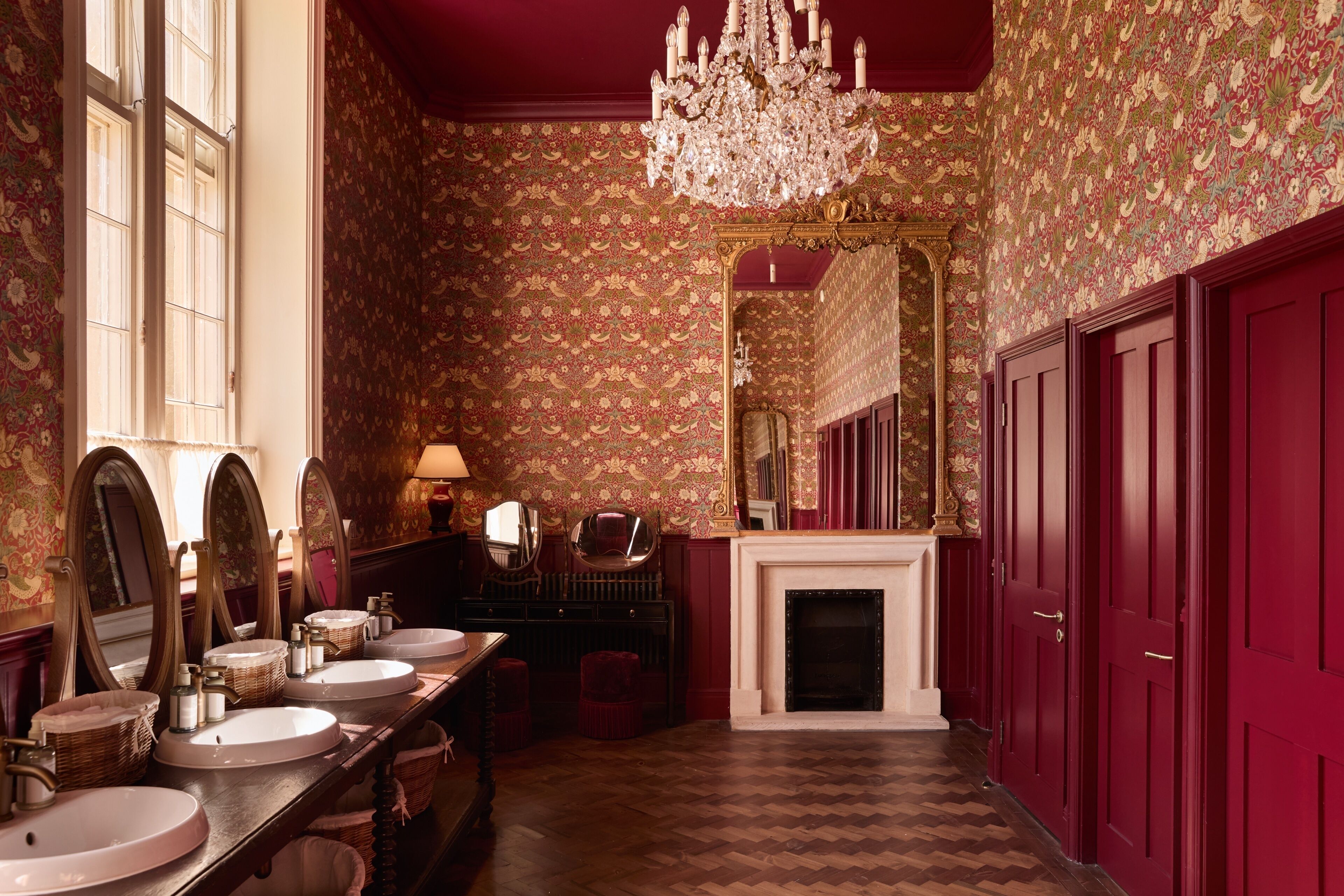 A luxurious bathroom with multiple sinks, a large mirror, a chandelier, and a fireplace.