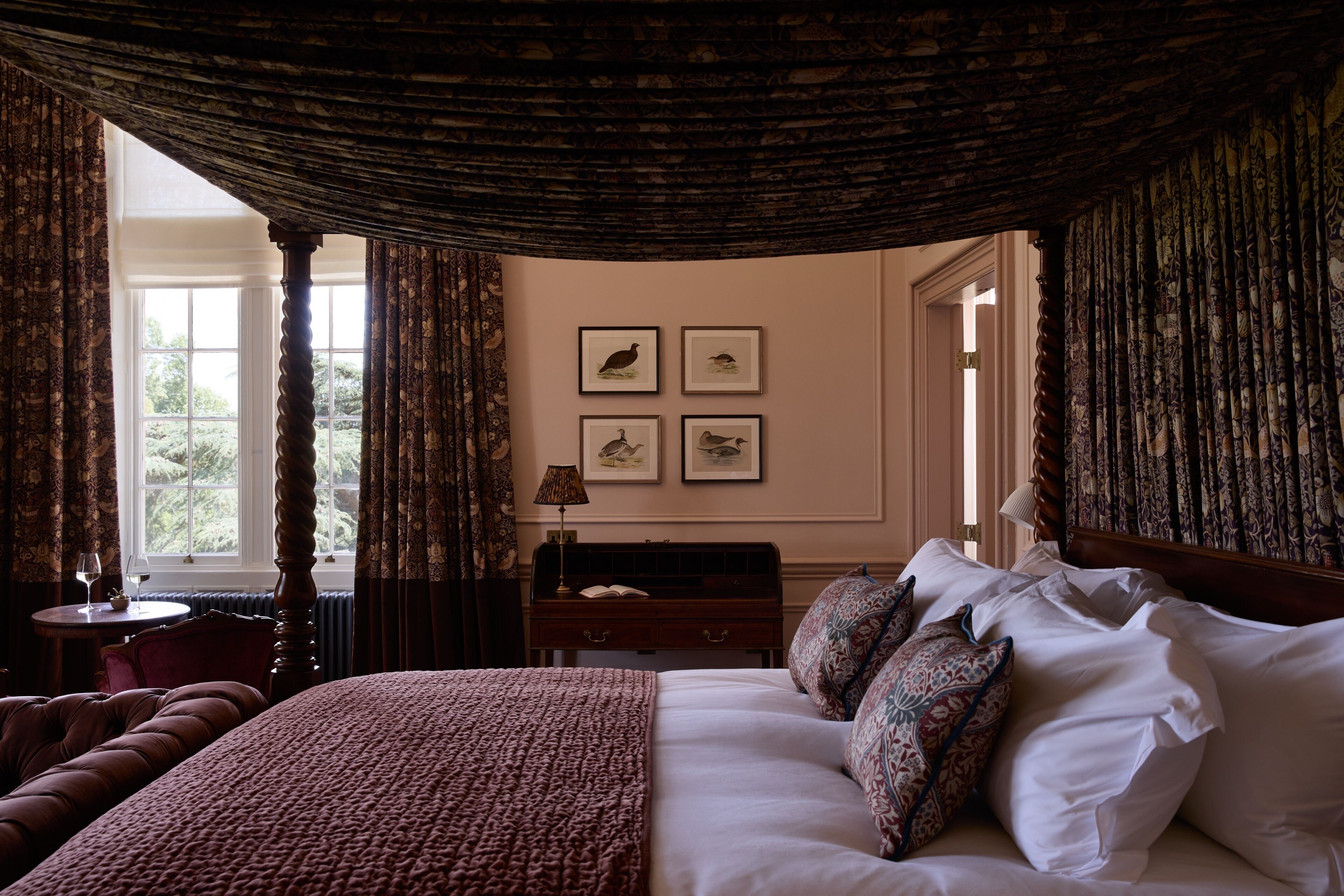 A bedroom with a large bed, a nightstand, a lamp, a chair, and a window with curtains.