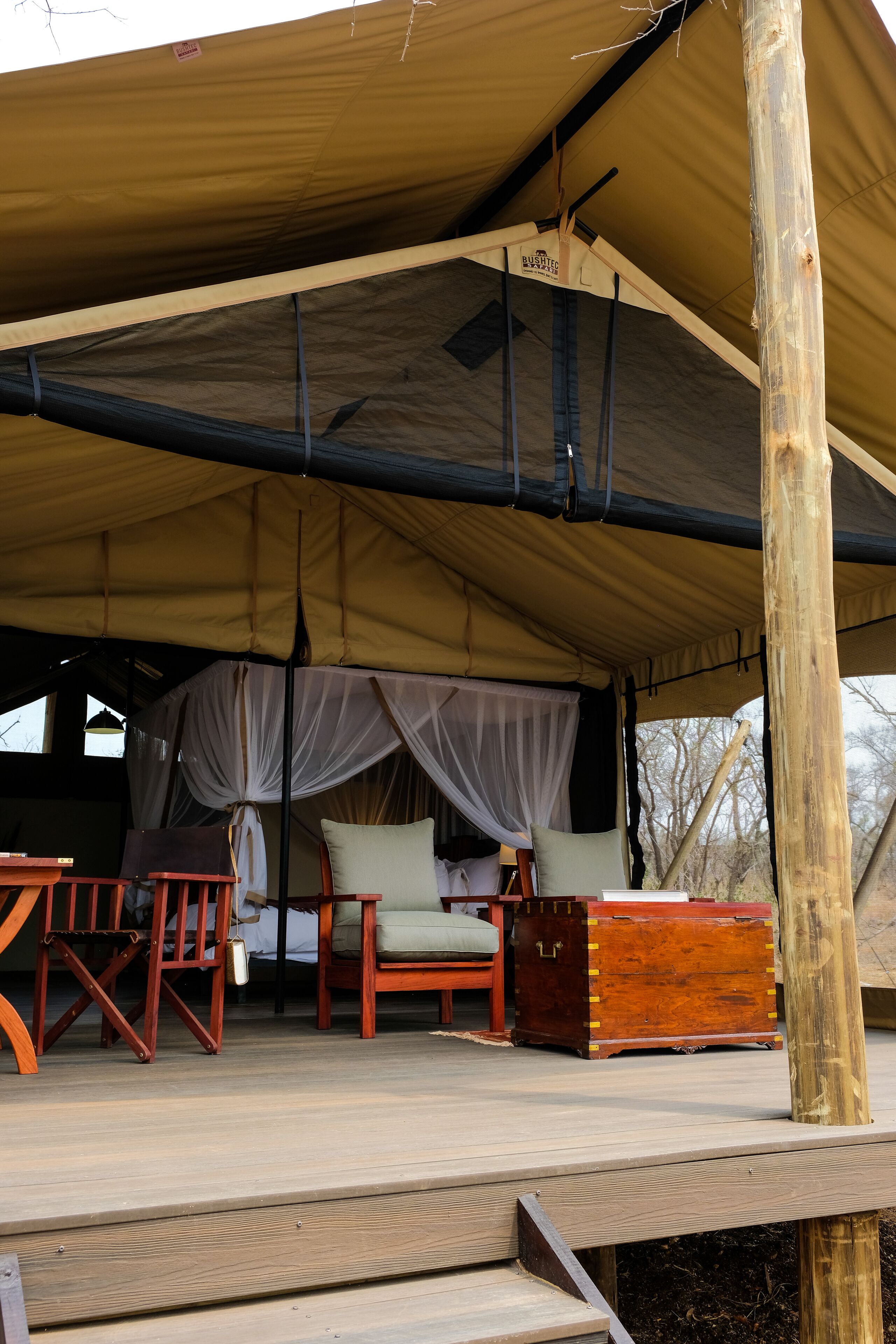 A covered outdoor seating area with a canopy, wooden furniture, and a storage chest.