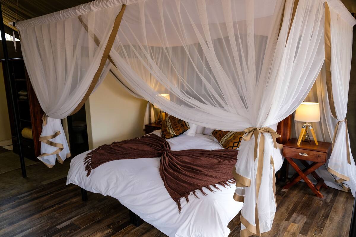 A bed with a canopy, wooden nightstands, and a lamp.
