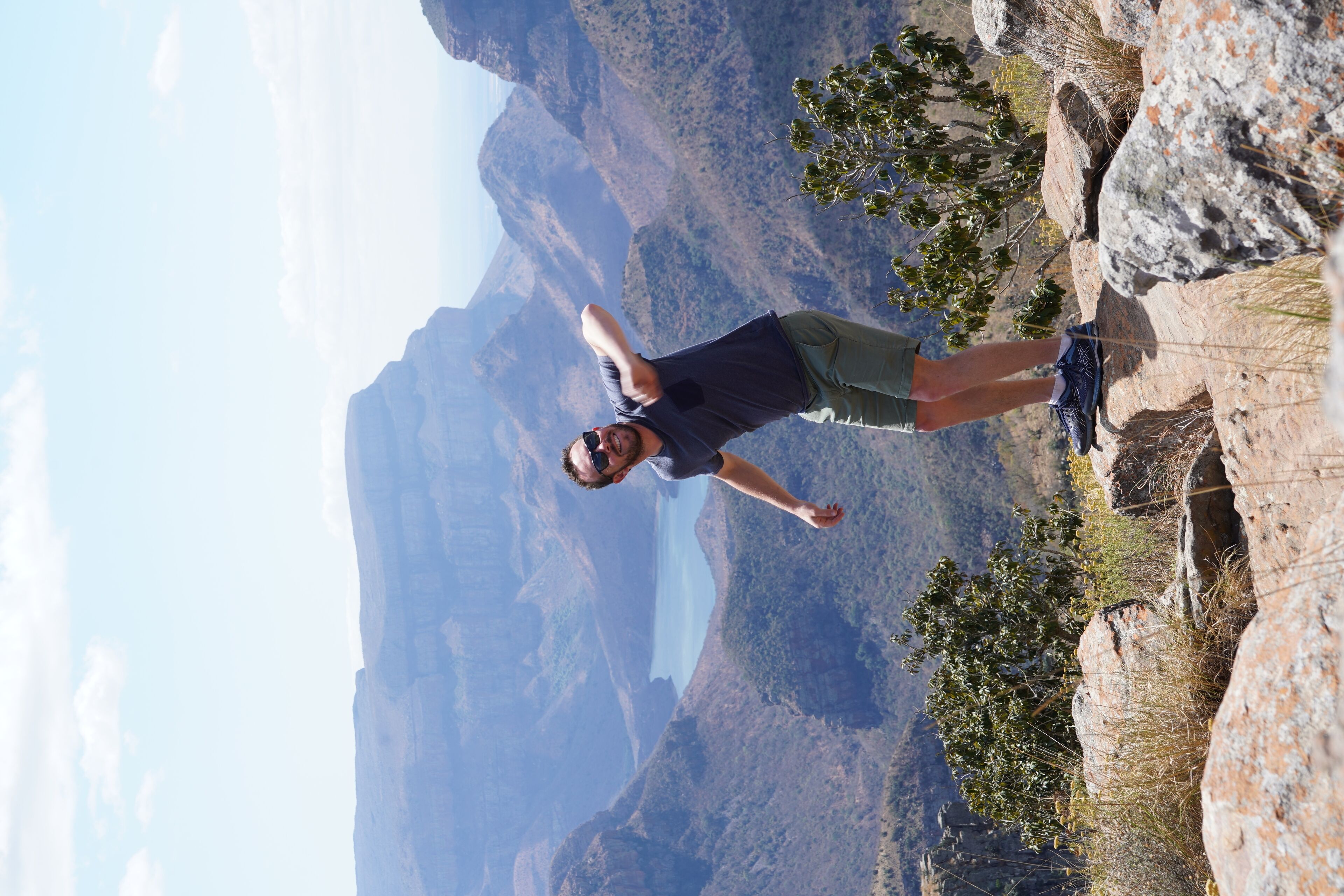 A person standing on a rocky outcrop with a mountainous landscape in the background.