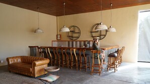 A spacious room with a leather sofa, a bar area with wooden stools, and a person standing near the bar. - Honeyguide Tented Safari Camps - Mantobeni (Bushbuckridge)