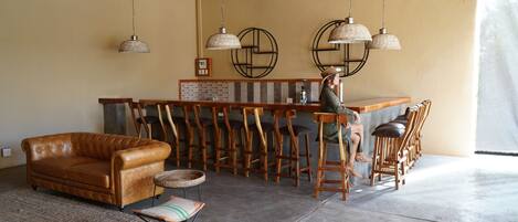 A spacious room with a leather sofa, a bar area with wooden stools, and a person standing near the bar.