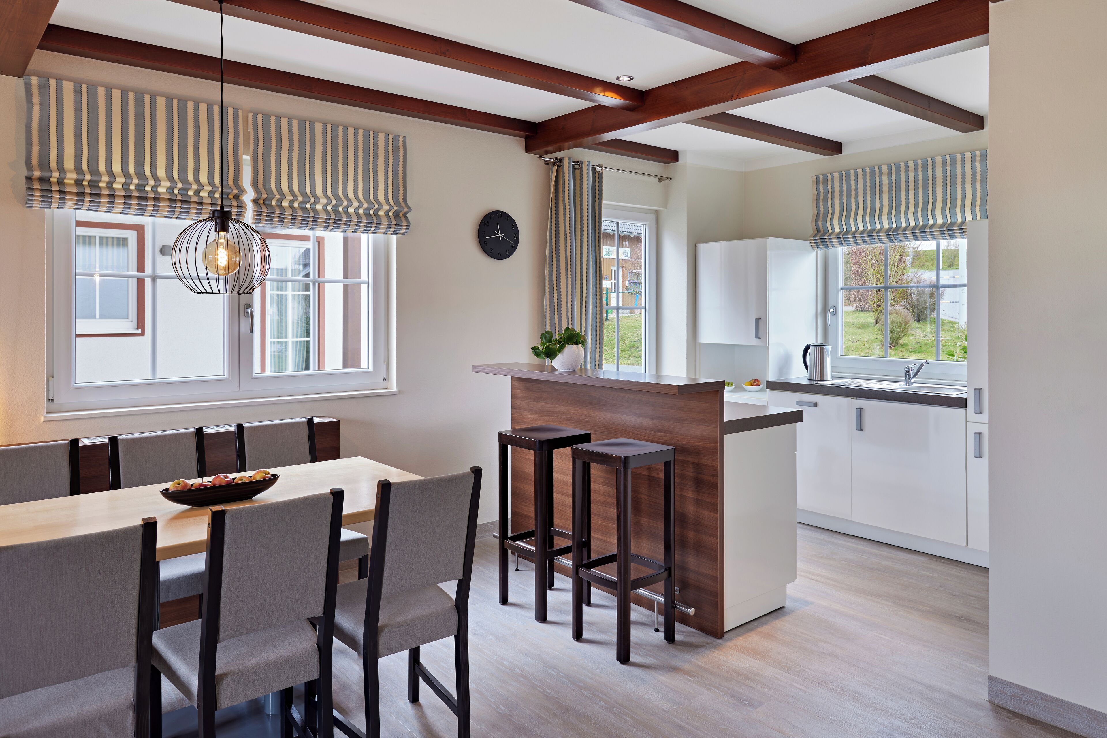 A modern kitchen with a wooden island, bar stools, and a dining area with a table and chairs.