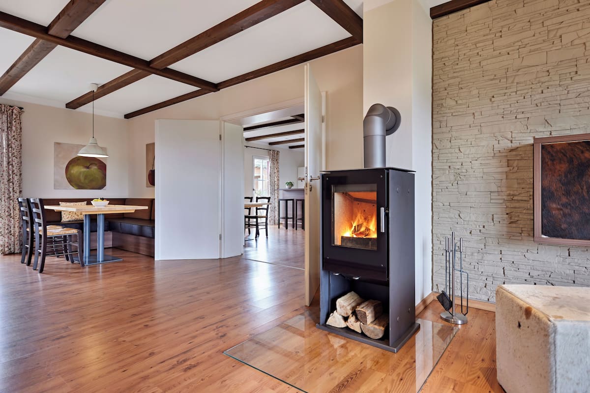 A modern living room with a wood-burning stove, wooden floors, and a stone wall.