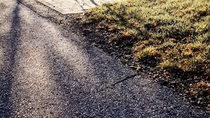 Una casa moderna de dos pisos con un balcón, un camino de entrada pavimentado y un pequeño árbol en primer plano.
