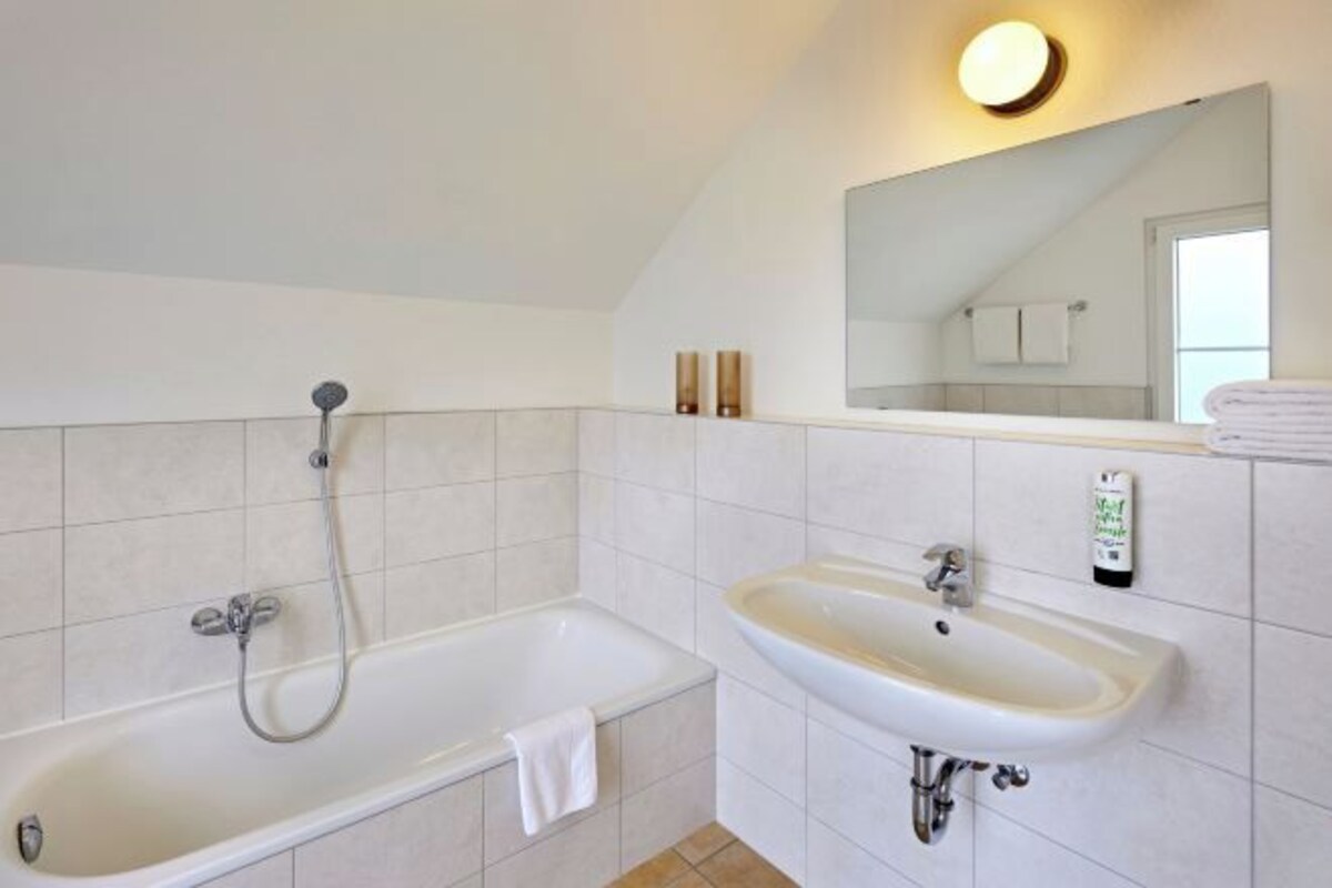 A bathroom with a bathtub, a sink, a mirror, and a towel rack.