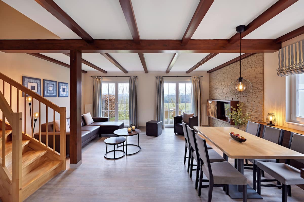 A spacious living area with a wooden staircase, a long dining table with chairs, a sofa, and a fireplace.