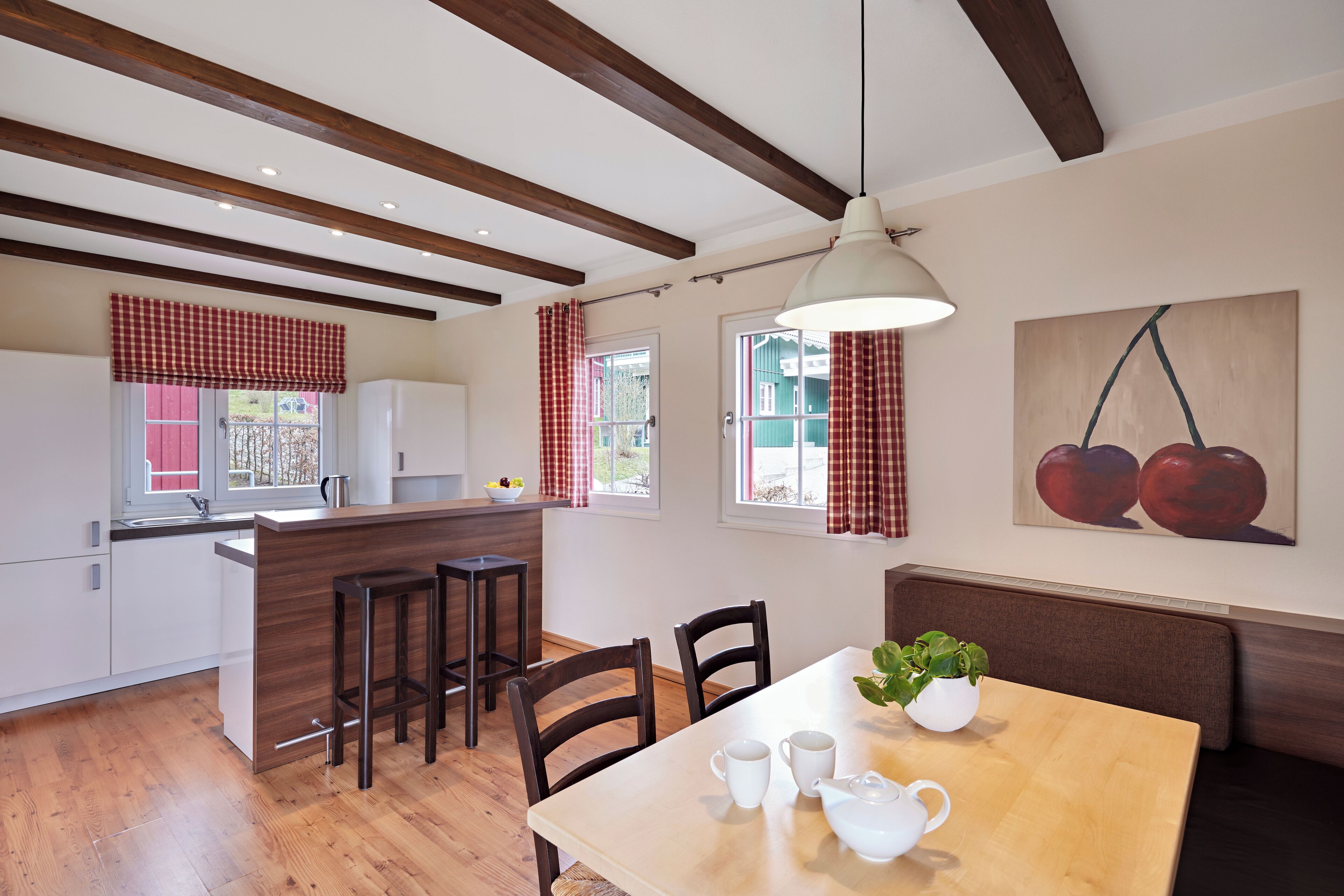 A modern kitchen with wooden beams, a dining area with a table and chairs, and a kitchen island with stools.