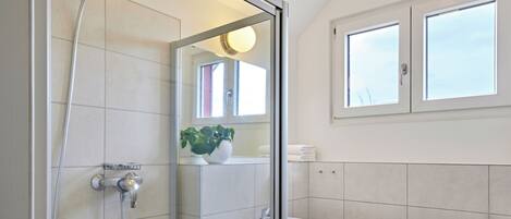 A modern bathroom with a glass-enclosed shower, a white sink, and a window above the mirror.