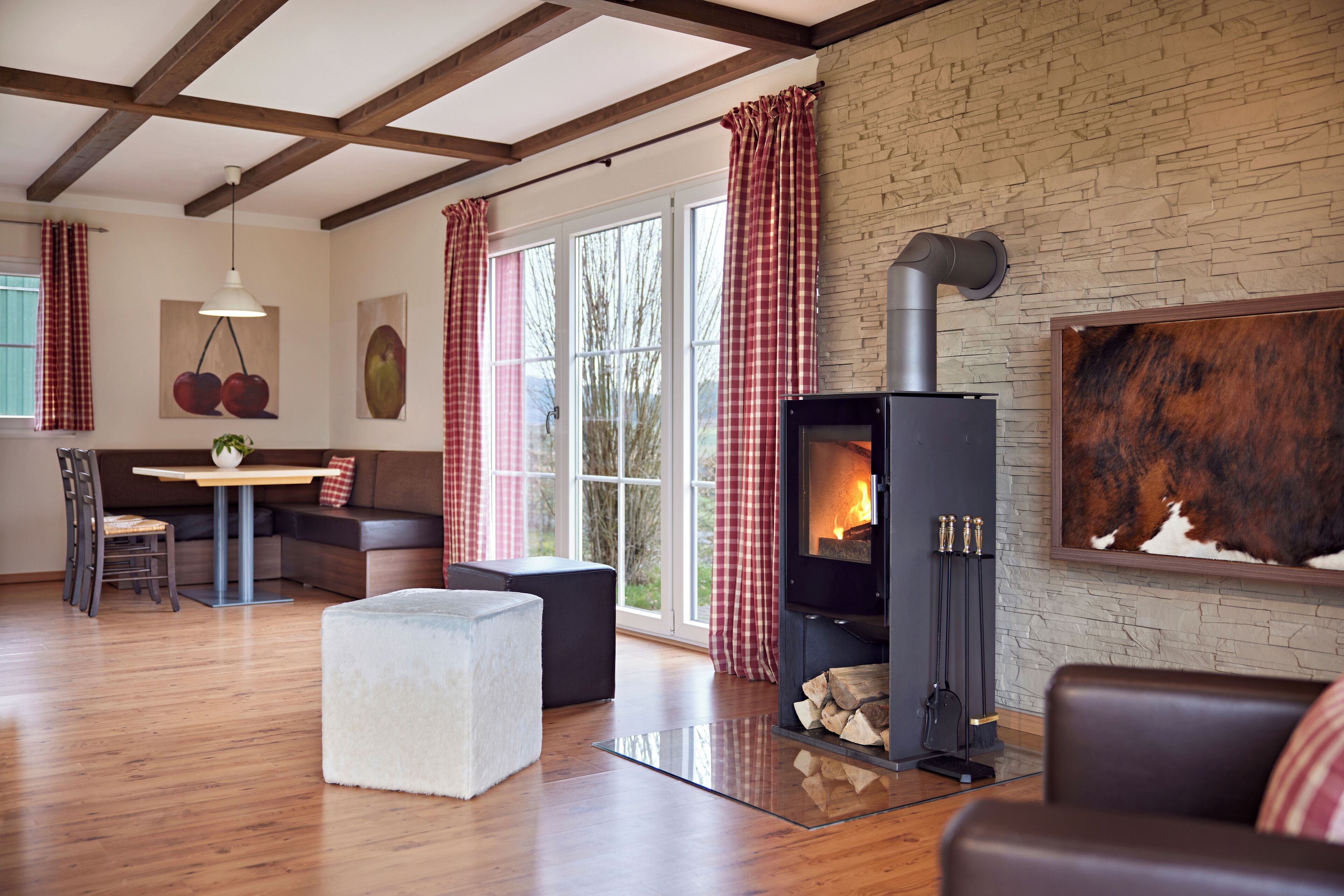Una sala de estar acogedora con chimenea, vigas de madera, pared de piedra y un gran ventanal con cortinas.