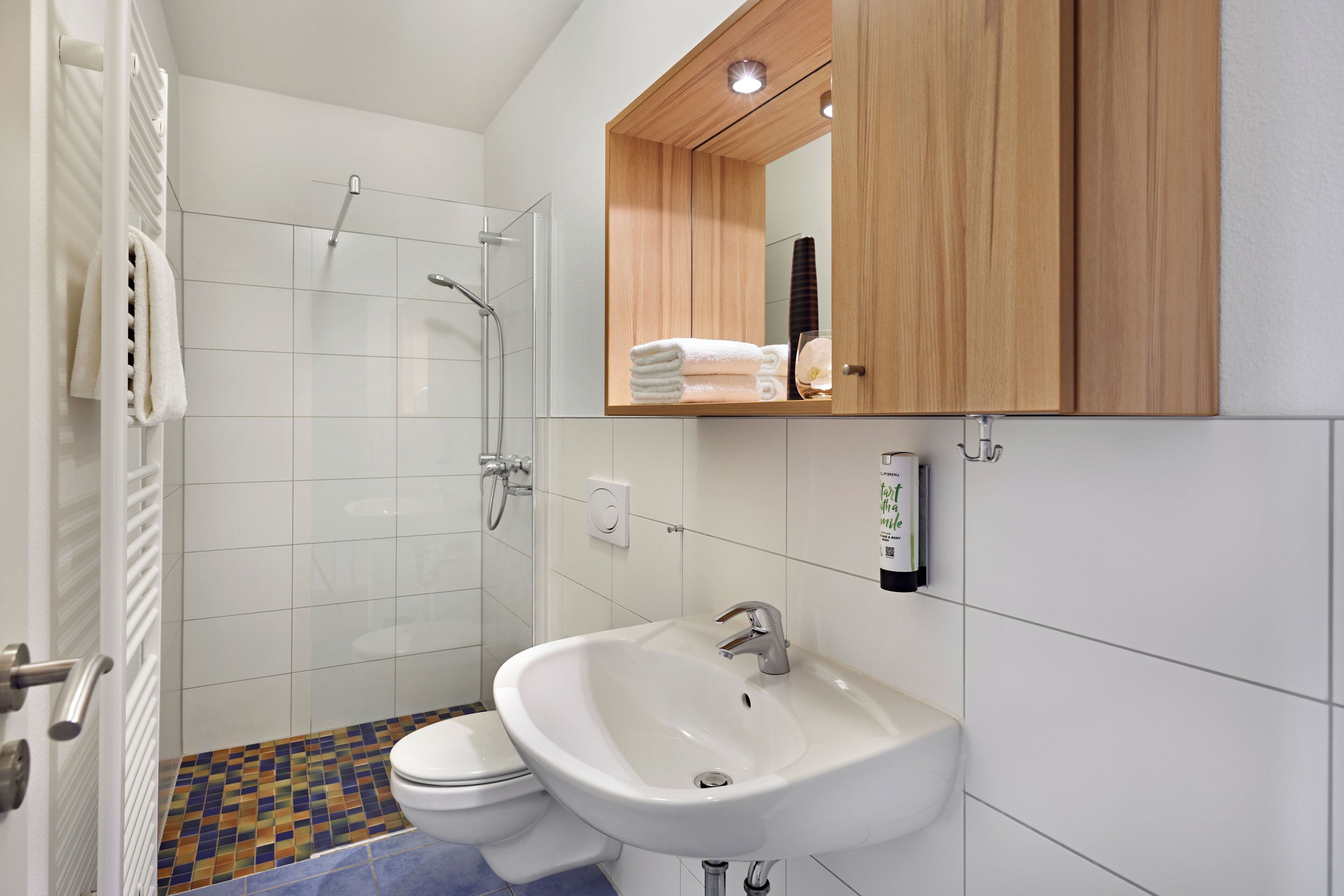 A bathroom with a shower, toilet, sink, and a mirror cabinet.
