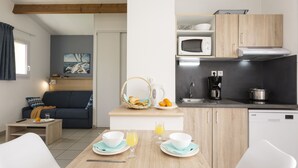 A compact living space with a kitchenette, a dining area with a table set for two, a sofa, and a painting on the wall. - Résidence Odalys Le Village des Amareyeurs (Le Chateau-d'Oleron)