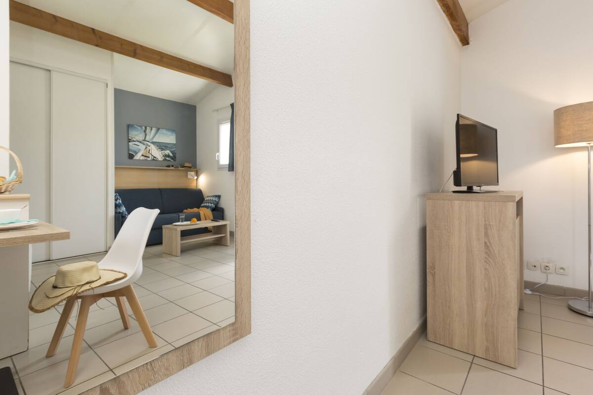 A modern living room with a large mirror, a TV on a wooden stand, and a floor lamp.
