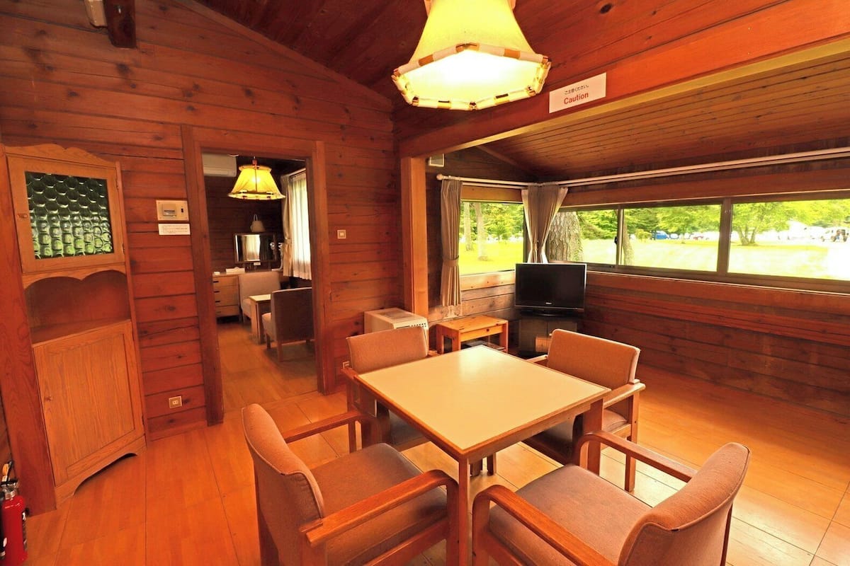 L’intérieur d’un chalet en bois comprend un coin repas, un téléviseur et une fenêtre donnant sur un paysage verdoyant.