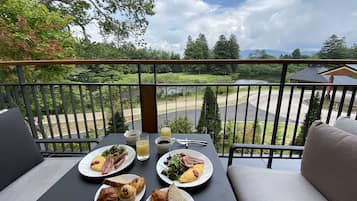 A balcony with a table set for breakfast, overlooking a road and greenery.