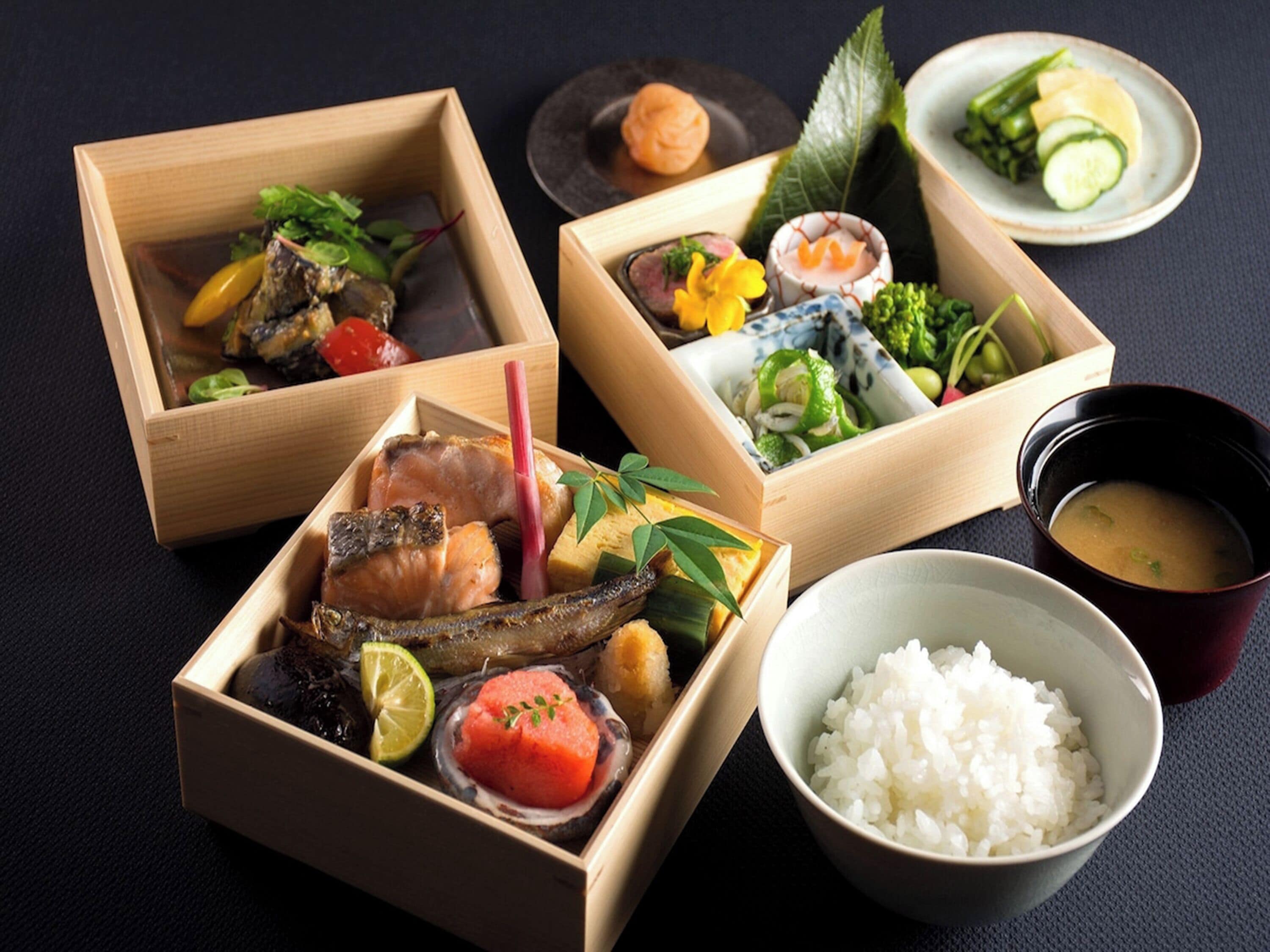 Tres cajas de madera con varios platos, un tazón de arroz blanco y un pequeño tazón de sopa.