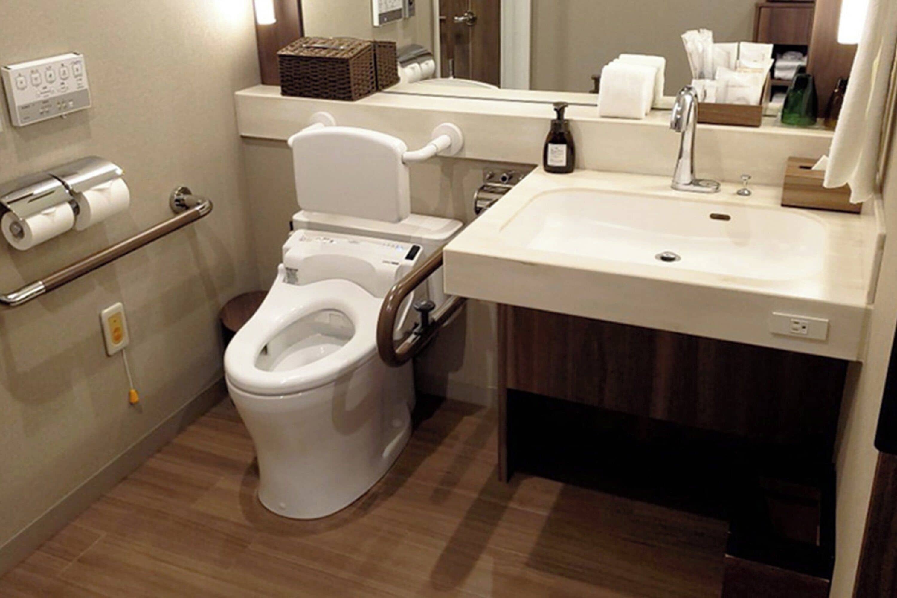 Un baño moderno con inodoro, lavamanos y barras de apoyo.