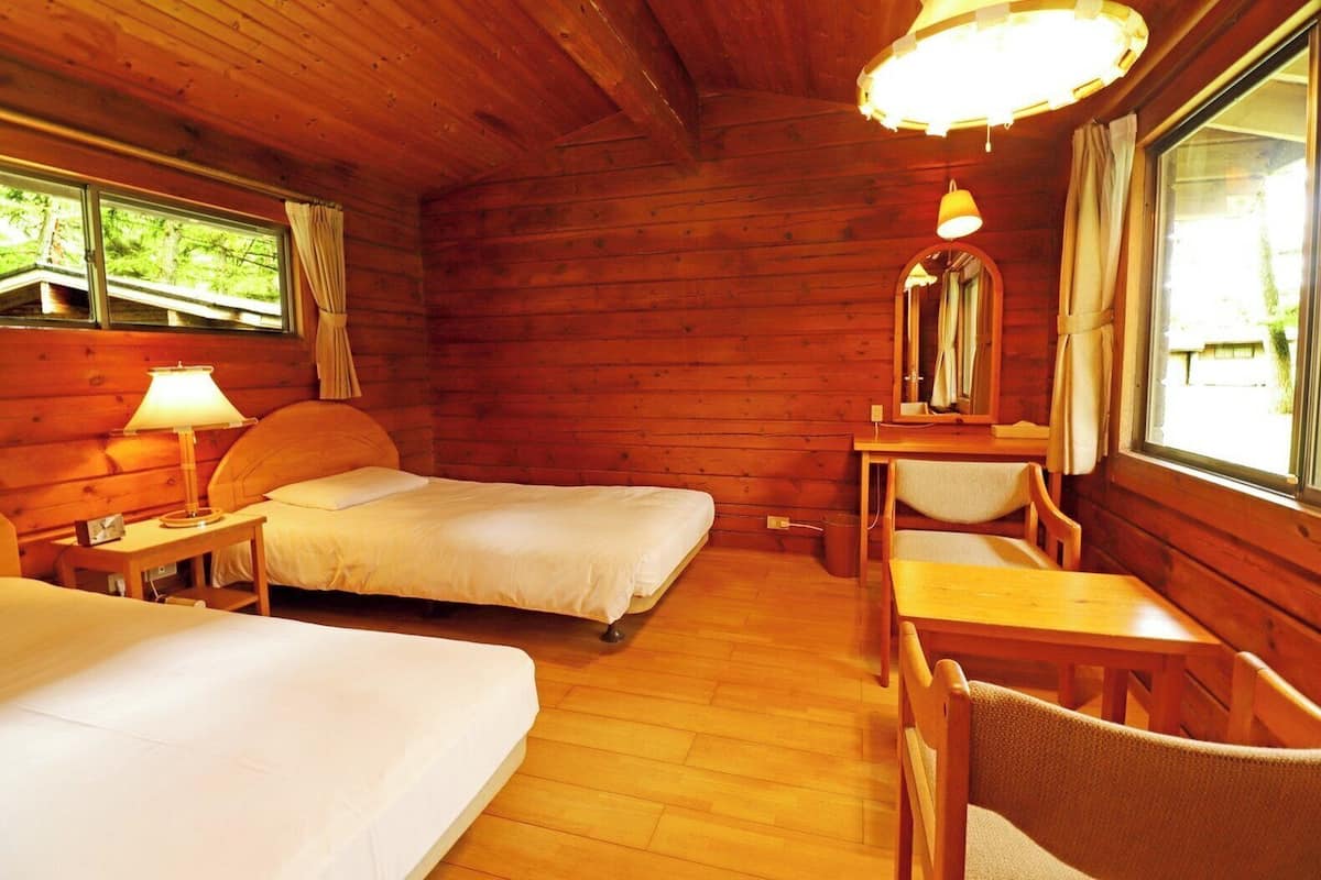 Une pièce de cabane en bois comprenant deux lits, une table, des chaises, une lampe et un miroir.