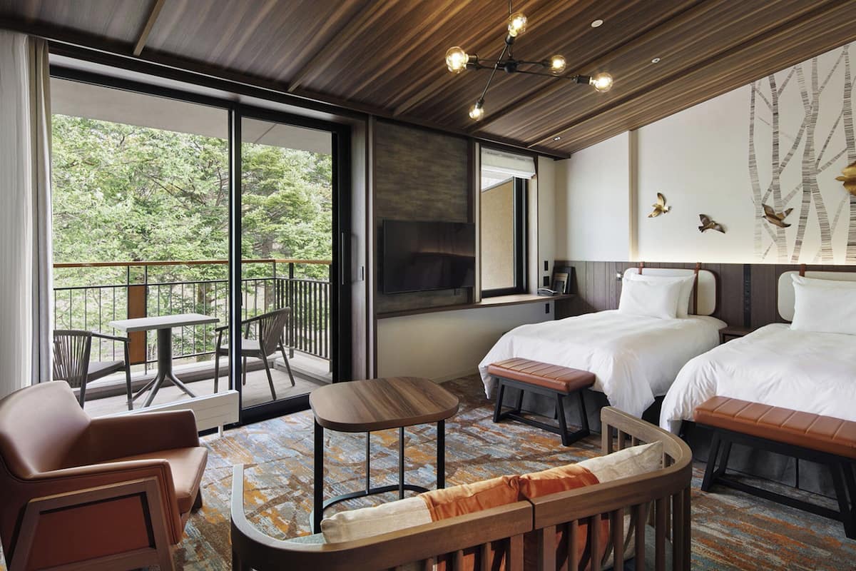 Une chambre d’hôtel avec deux lits, un canapé, une petite table et un balcon équipé d’une table et de chaises.