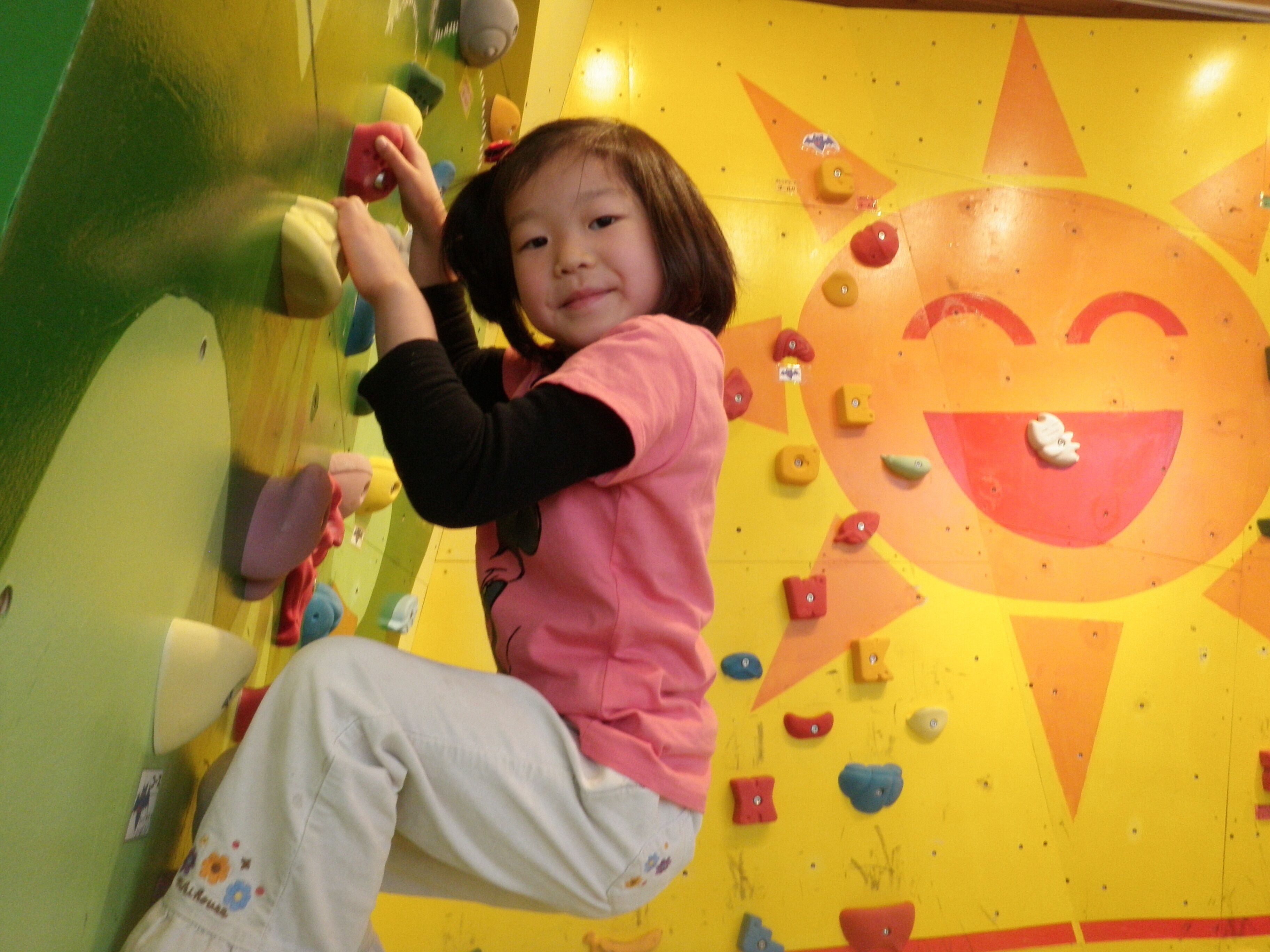 Un niño trepando por una pared de colores con un diseño de sol sonriente.