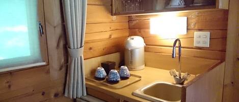 Cocina compacta con paredes de madera, un lavamanos pequeño, una cafetera y un escurreplatos.