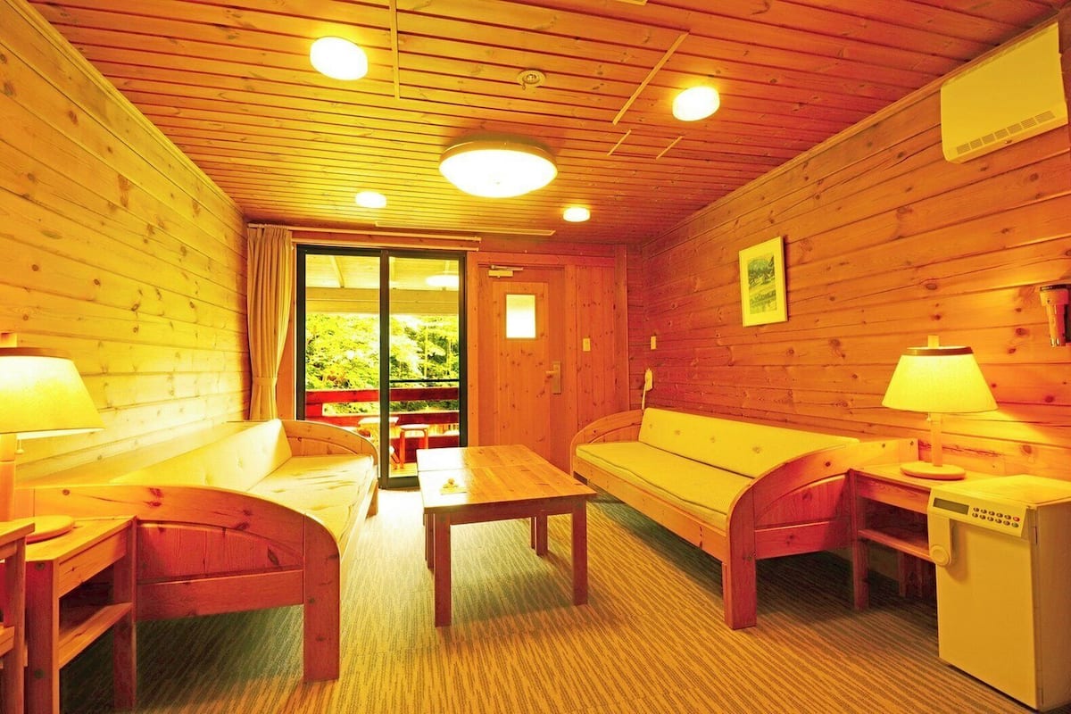Une cabane chaleureuse aux murs et au plancher en bois, avec un canapé, deux fauteuils, une table et un petit réfrigérateur.