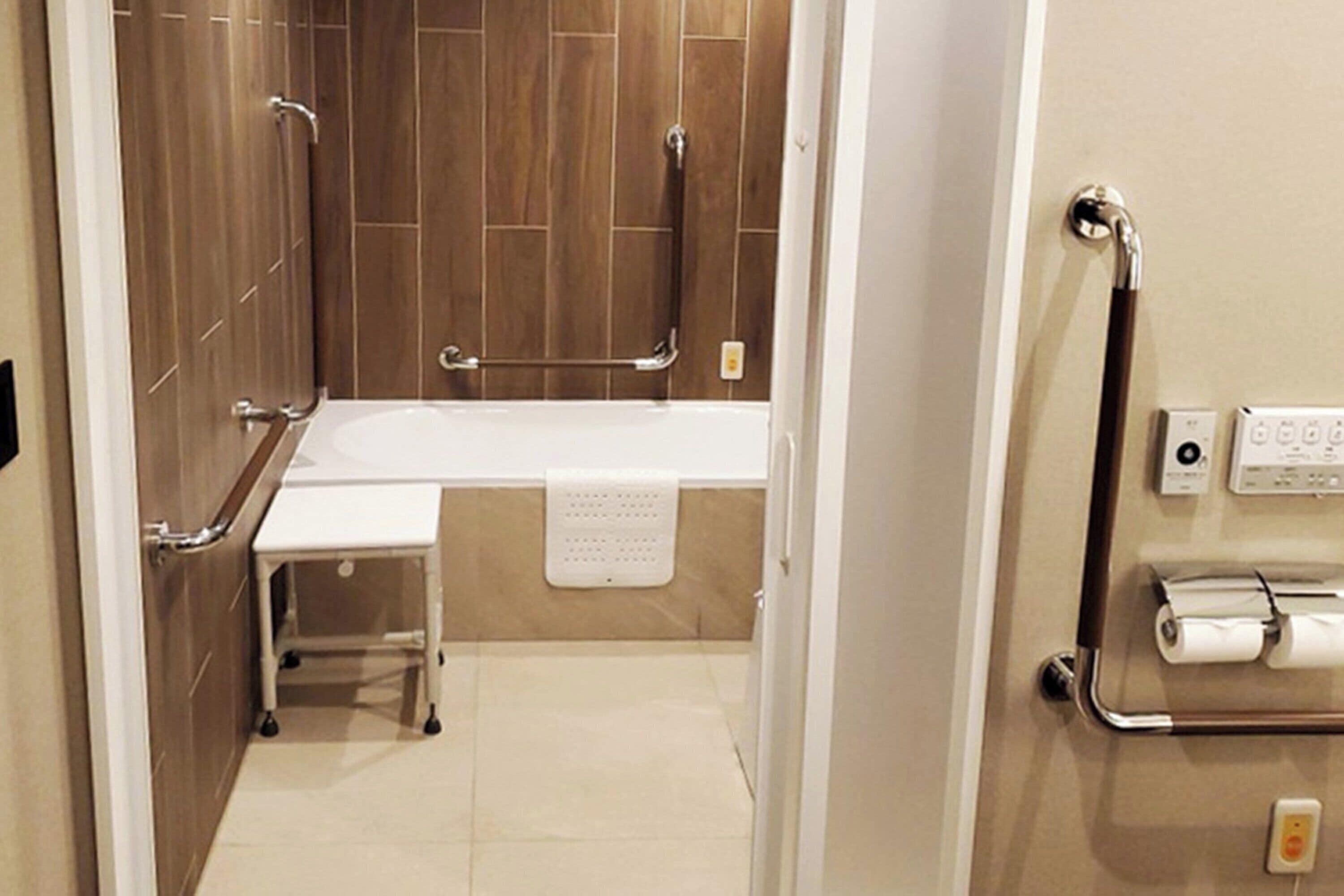 Un baño con una bañera blanca, barras de apoyo, un perchero y un dispensador de papel higiénico.