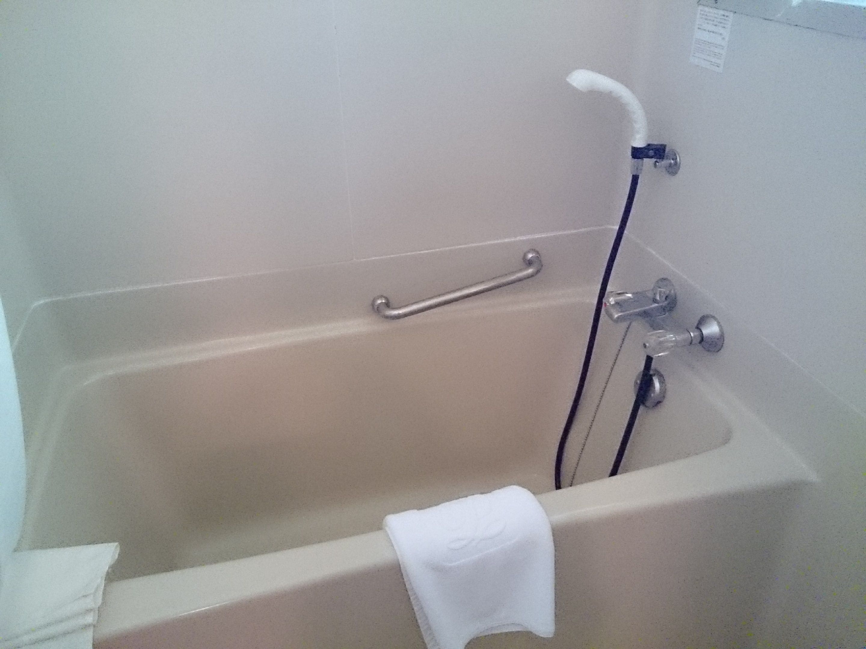 A bathtub with a grab bar, a towel, and a shower hose.