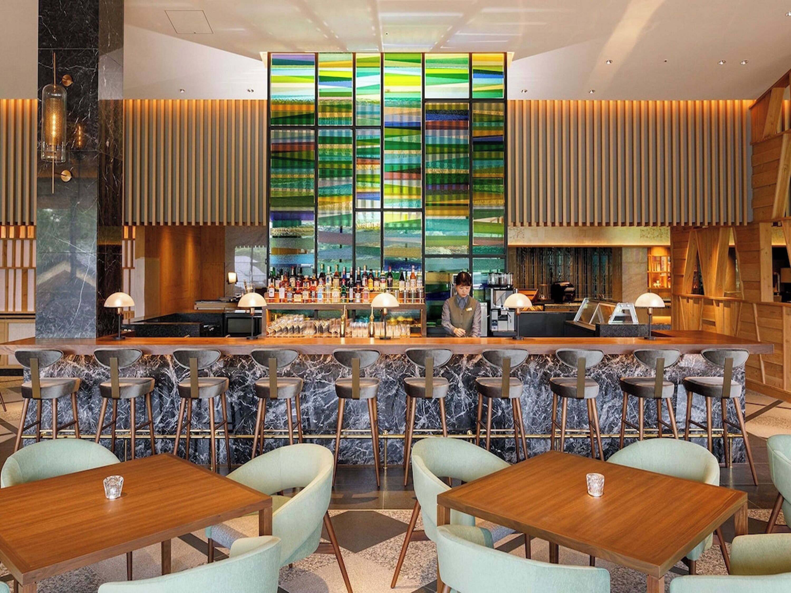 A modern bar area with a bartender, bar counter, and seating with tables and chairs.